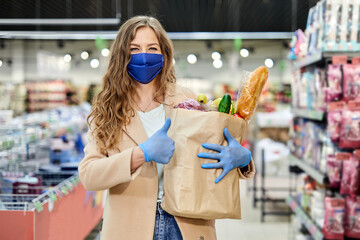 Woman in a medical mask holds a paper bag with products, vegetables and sign thumb up . Shopping during the covid-19 pandemic.