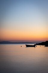 A splendid orange-blue evening sky is reflected after sunset in the smooth sea on which a small motorboat lies at a buoy.