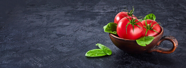 Fresh grape tomatoes with spinach Leaves on black stone background. Vegan veggies diet food. Herb, red tomatoes, cooking concept.