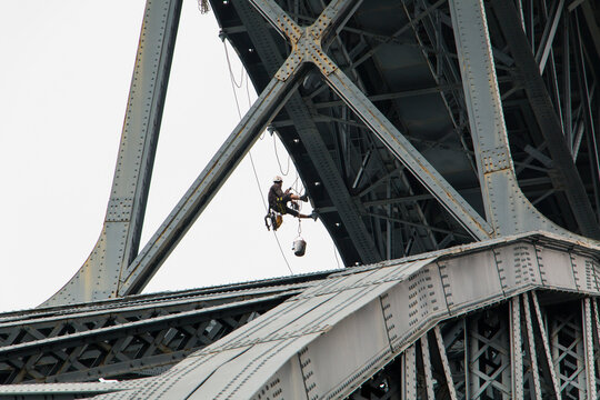 Fototapeta Painter working on the Porto Bridge. A worker repairs the Porto bridge hanging by ropes