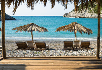 Sunbeds with parasol on the beach in Skopelos with sunny holiday atmosphere with turquoise clear sea and blue sky.