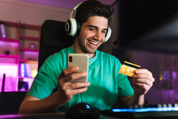 Image of man holding credit card and cellphone playing video game