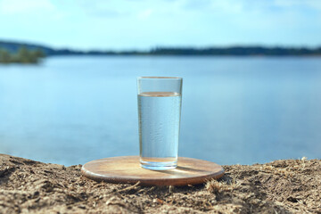 Fototapeta na wymiar Clear fresh water in a glass against background of river or lake. Healthy food and environmentally friendly water.