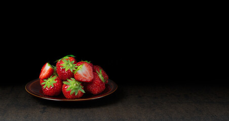 A brown plate  with fresh red juicy strawberries from Belgium isolated against a dark background with space for text.