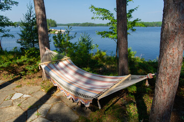 Summer on the lake. Colourful Empty hammock between two trees with the view of the blue water.