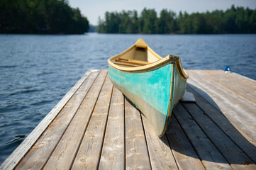 Green canoe rest on a lake wooden pier on a sunny summer day at the cottage. A wood pier is visible...