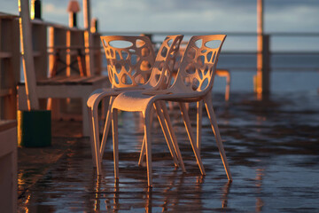 Wet plastic chairs after the rain on the shore illuminated by the sunset light