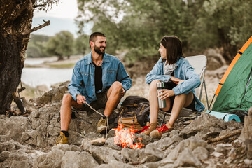 Naklejka na ściany i meble Romantic couple sitting by bonfire. Beautiful couple in love enjoying at campsite.