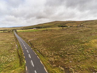 Aerial drone view on a small country road in a West of Ireland. Fields on each side, Cloudy grey sky.