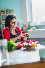 Portrait of a middle-aged woman preparing vegetables at her kitchen table. She's peeling a zucchini.