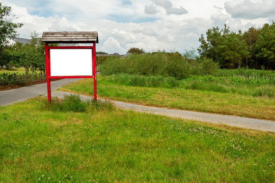 Red wooden billboard with clean white space for text in a park on green grass by a small walking path