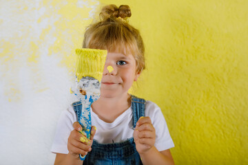 Cute little toddler girl painting the wall with yellow color in new house. Family repair apartment...