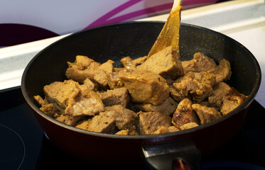 Stir the fried meat in the pan with a wooden spatula.Meat on a plate with green salad and rice.Delicious and healthy food.