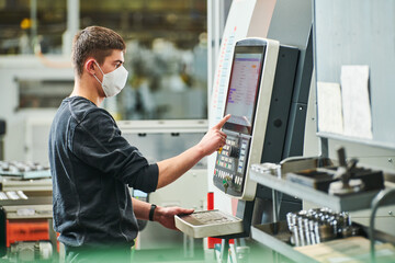 Industrial worker operating cnc machine in protective mask at metal machining industry