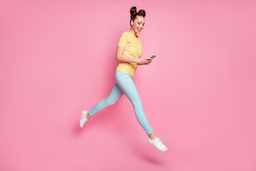 Fototapeta na wymiar Full size profile photo of attractive lady two buns hold telephone writing new blog post walk street jumping high up wear casual striped t-shirt pants shoes isolated pink color background