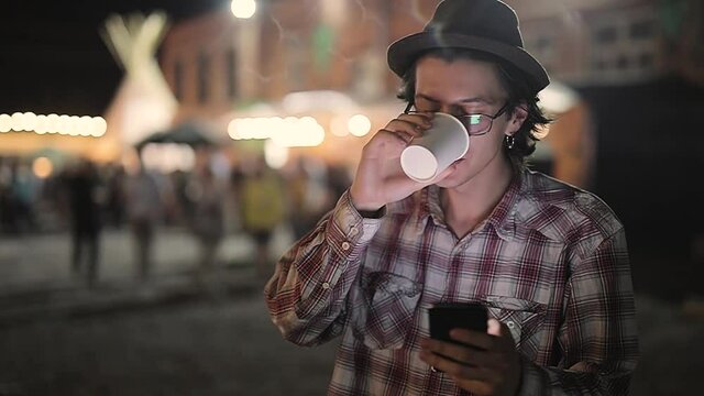 Young Man Drinking Coffee And Using Phone At Street In Evening, Stylish Male With Smartphone Outdoors