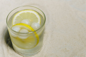 transparent glass with ice and sparkling water on the sand on a blue background