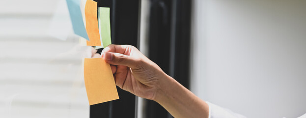 Cropped image a hand is holding an empty sticky note at the glass wall.