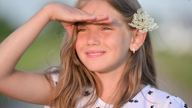 Portrait of a Cute School-Age Girl in the Evening Park. A beautiful girl in a dress walks in the field at sunset. happy childhood concept. Childhood Moment.