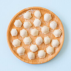 Raw homemade ravioli on a wooden plate. Top view.