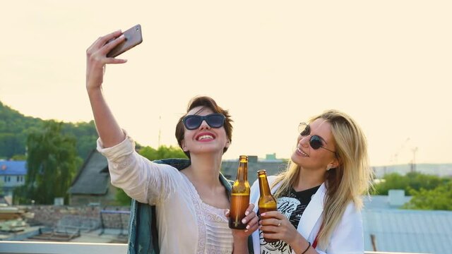 Happy Women Making Photo On Phone Outdoors, Drinking Beer And Doing Selfie 