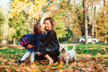 Fototapeta premium Fashionable mother and schoolgirl walking with their dog in park. Autumn time, weekend and holidays.