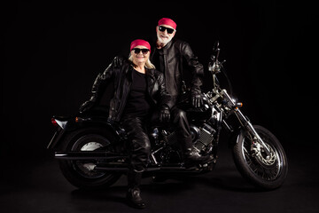 Obraz na płótnie Canvas Photo of aged bikers grey haired man lady soulmates couple sitting on vintage chopper feel young going rock festival wear rocker leather jacket pants bandana isolated black color background