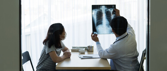 doctor looking at chest x-ray of the asian woman patient who come and visit at check up clinic in...