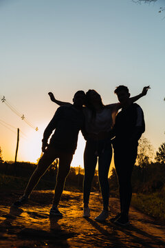 Friends hug at sunset on the road.  They enjoy the golden hour in their millennial lifestyle