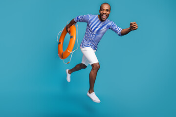 Full length body size view of his he nice handsome cheerful glad guy rescuer sailor jumping carrying rubber lifesaver running hurry rush isolated over bright vivid shine vibrant blue color background
