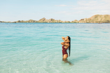 Woman in red swimsuit enjoying in transparent turquoise ocean water with mountain view. Travel and vacations concept. Beauty and wellness. Tropical background with empty space.