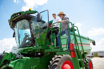 Professional farmer with a modern tractor, combine at a field in sunlight at work. Confident, bright summer colors. Agriculture, exhibition, machinery, plant production. Senior man on his machine with © master1305