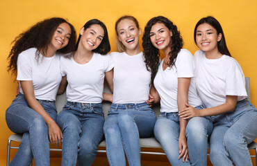 Cheerful Girls Friends Hugging Sitting On Bench On Yellow Background