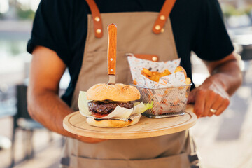 Waiter serving a delicious burger, fries and sauce served on wooden boards.