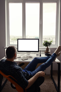 Man Relaxing While Working Remotely From Home Holding Legs On The Table Looking At The Computer Stretching Hands Behind His Head