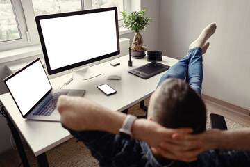 Man relaxing while working remotely from home holding legs on the table looking at the laptop,...