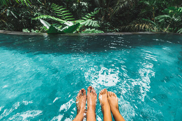 Couple feet together in luxury swimming pool with turquoise clear water outdoors with jungle view. Tropical Honeymoon, leisure vacations.