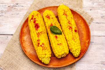 Boiled corn cobs on ceramic plate. Sea salt, fragrance paprika, fresh basil leaf