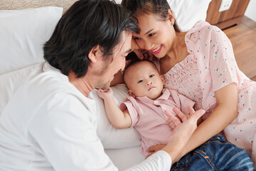 Obraz premium Happy young Asian couple enjoying spending time with little son, lying on comfy bed at home