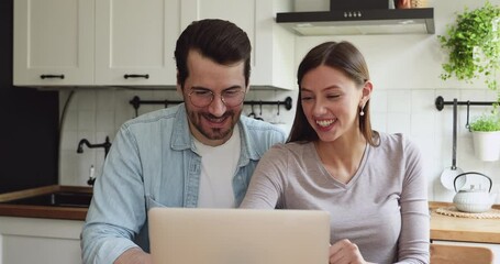 Young couple spouses sit on home kitchen together watching sport match on laptop celebrating favourite team win scream with joy feels excitement. Great news, on-line gambling betting victory concept - Powered by Adobe