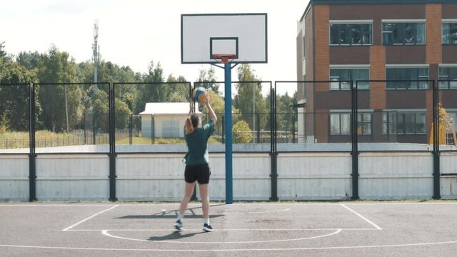 Close up of female professional basketball player making slam dunk during basketball game in floodlight basketball court. The player is wearing unbranded sport clothes