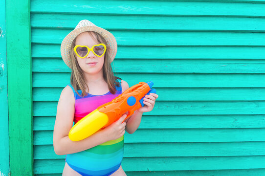 Girl with a water gun. Baby in hat and glasses on a wooden background.