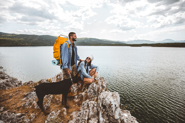 Hikers with backpacks and their doberman  sitting on cliff enjoying at the mountain lake