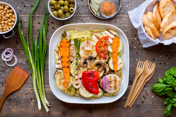 Dinner table with assorted grilled vegetables, bread and snacks on wooden background, top view