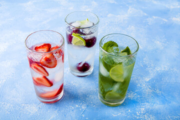 Fototapeta na wymiar Three glass of refreshing cool detox drink with strawberry, lime, cherry and mint on blue background. Various summer lemonades or ice tea. Mojito cocktails with ice cubes. Healthy eating. 