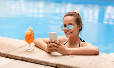 Attractive young woman with cellphone chatting online in swimming pool outside
