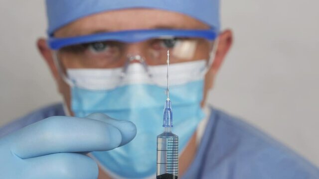 A syringe with a vaccine. A medical solute in the hands of the doctor. The doctor in the medic face mask is preparing an injection. Close up view