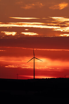 A silhouette of a distant windmill in front of a buring sky