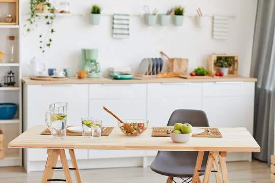 Background image of wooden dining table with fresh food ingredients and salad bowl in cozy kitchen interior, copy space