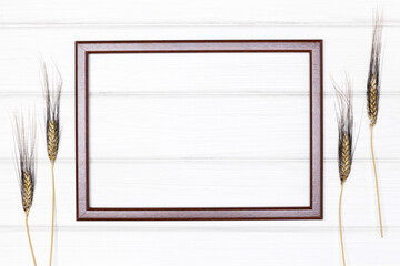 Empty wooden picture frame on white painted wood boards with wheat stems ears. Creative rustic mockup background
